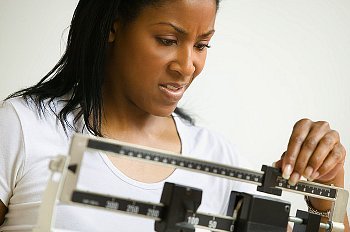 A woman weighing herself and frowning at the scale